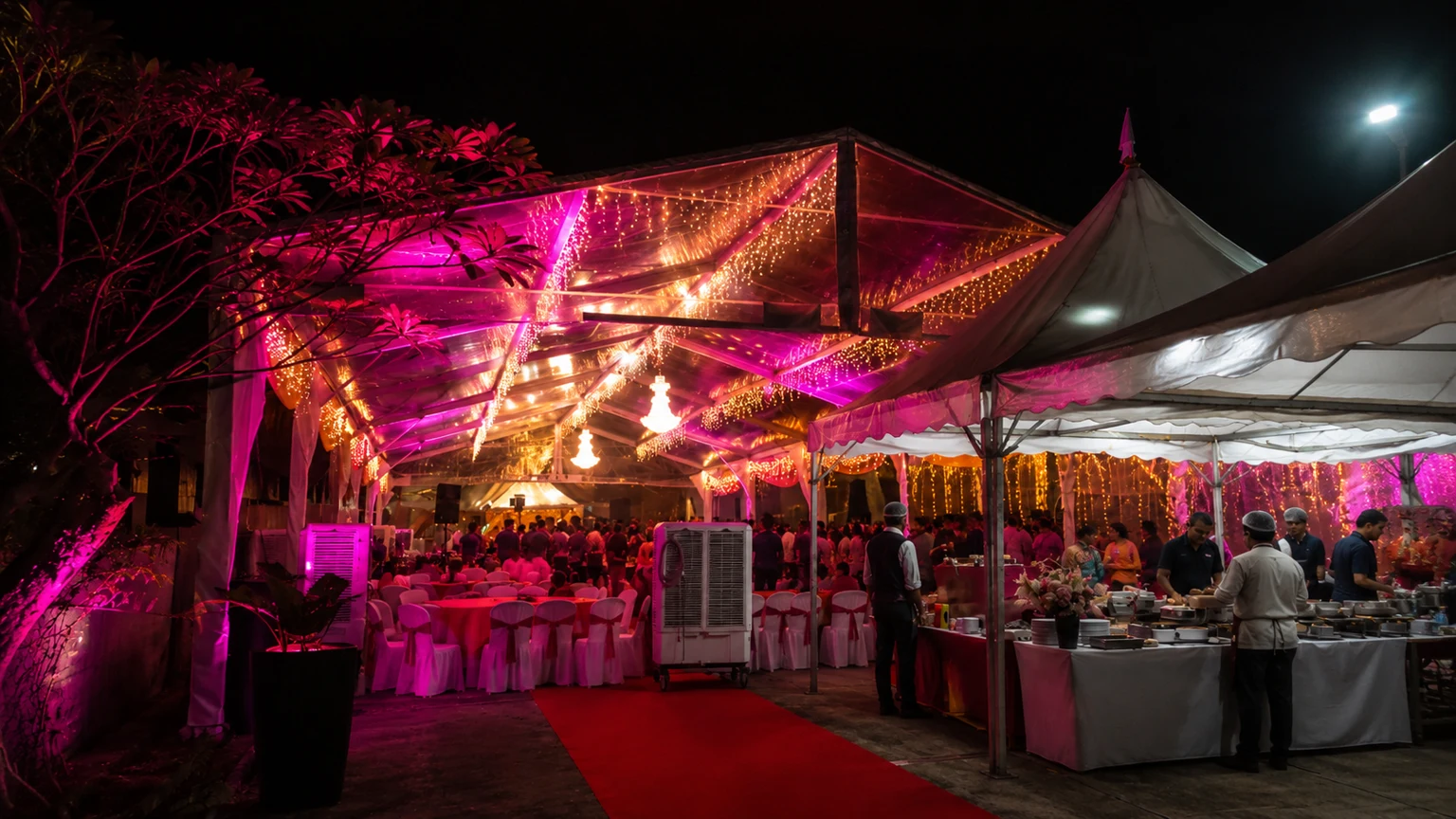 Company event buffet setup beside a transparent marquee with pink lighting, red carpet entry, catering counters, guest seating and night event lighting